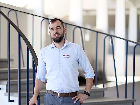 Mann in weissem Hemd und grauen Hosen steht auf einer Treppe.",