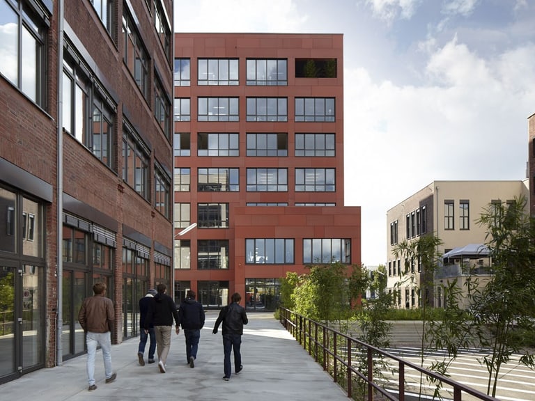 Menschen gehen auf Gehweg zwischen modernen Gebäuden.