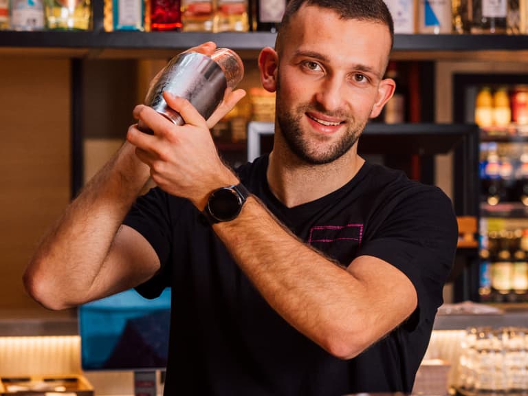 Barkeeper hält Shaker hinter der Bar mit Getränken im Hintergrund.