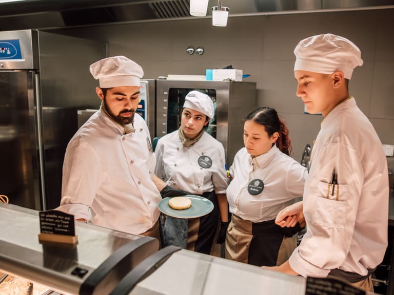 Köche in einer Restaurantküche diskutieren über Präsentation eines Gerichts auf einem Teller.