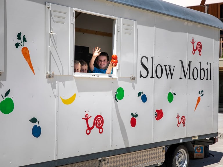 Zwei Personen winken aus dem Slow Mobil Fahrzeugfenster.