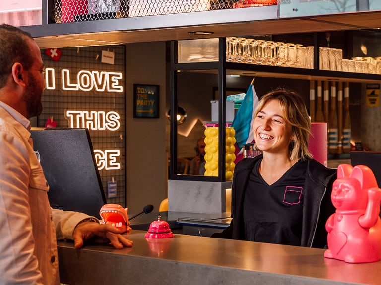 Frau lächelt an Rezeption mit Mann gegenüber und Dekoration im Hintergrund.