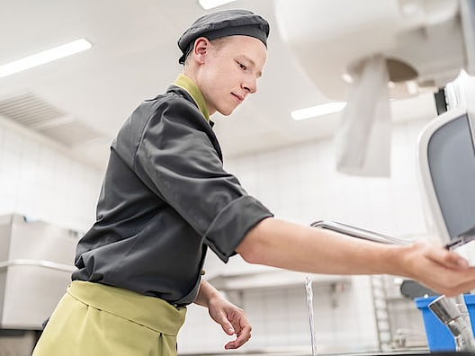 Mitarbeiter in der Küche wäscht seine Hände nach den SV Hygienevorschriften.