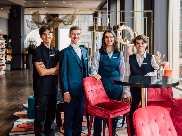 Vier Jugendliche in Restaurantuniformen posieren am Tisch in einem modernen Restaurant.