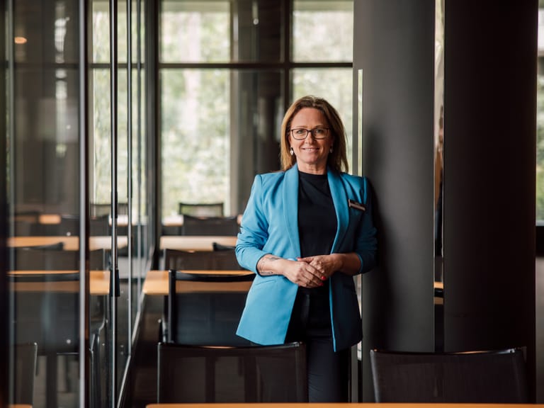 Geschäftsfrau in blauem Blazer steht lächelnd im Büro.