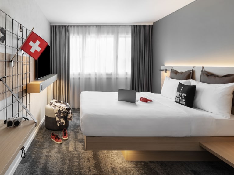 Modernes Hotelzimmer mit Schweizer Flagge und eingefahrenem Laptop auf Bett.