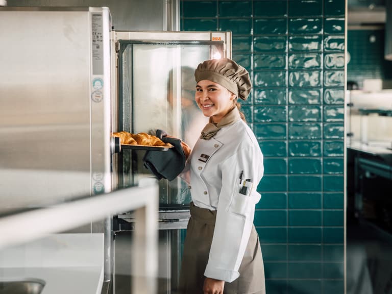 Köchin nimmt Croissants aus dem Ofen in der Küche heraus.