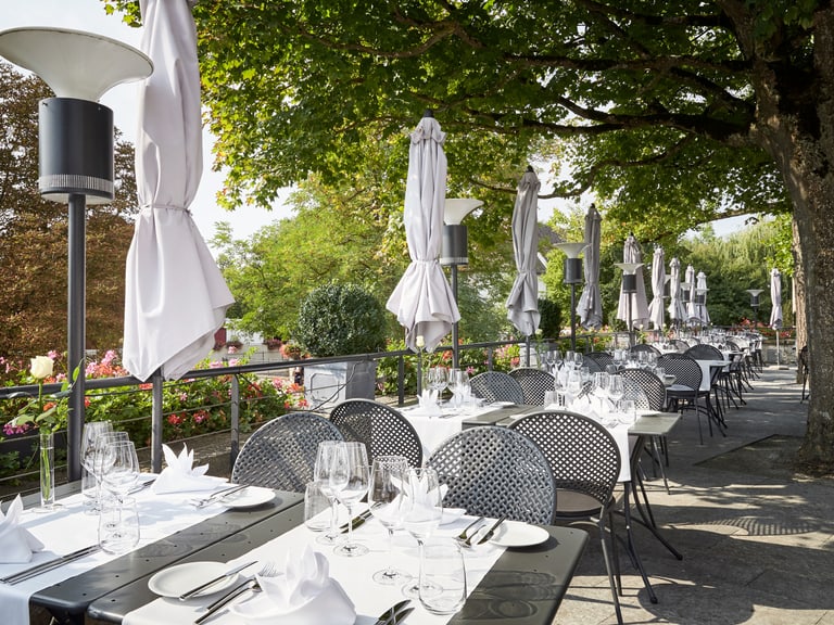 Sommerterrasse auf dem Schloss Laufen am Rheinfall unter Bäumen und weiss gedeckte Tische.