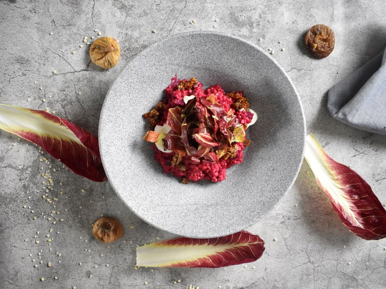 Grauer Teller mit buntem Gericht, umgeben von Radicchio und getrockneten Feigen.