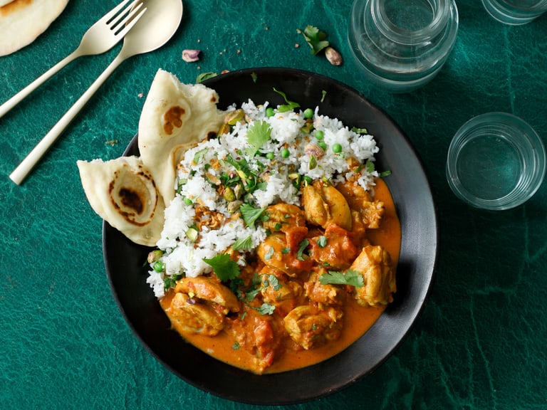 Indisches Curry mit Reis und Naan-Brot auf dunklem Teller, ebenerdig fotografiert.