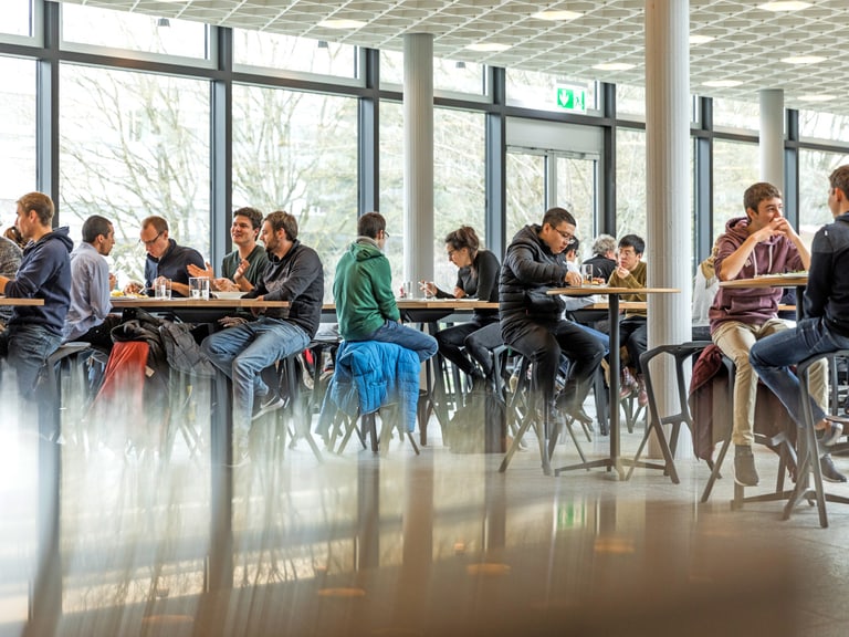 Studentinnen und Studenten sitzen in der hellen und modernen Mensa und geniessen ihr Mittagessen.