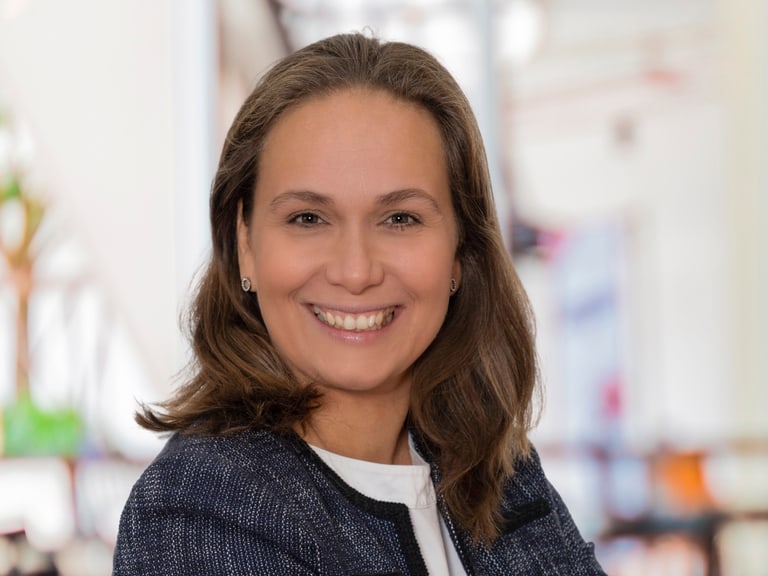 Lächelnde Frau mit gekreuzten Armen in einem Geschäftsumfeld.