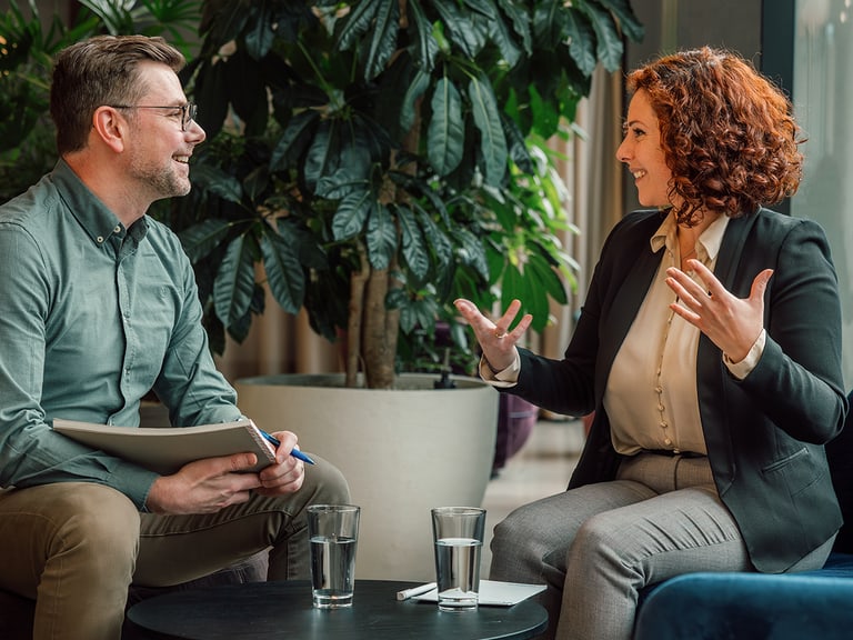 Mann und Frau bei Gespräch in modernem Büro, Pflanzen im Hintergrund.