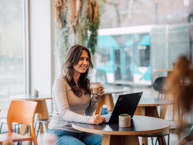 Frau mit Laptop und Kaffee sitzend an einem Café-Tisch.