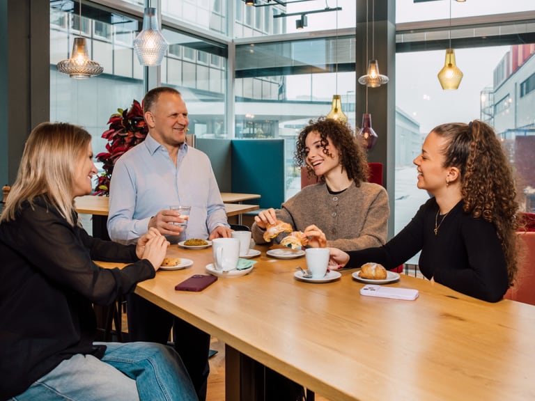 Vier Personen unterhalten sich bei Kaffee und Gebäck an einem Tisch im Café.