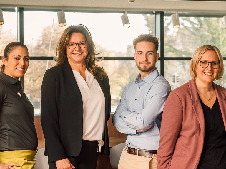 Vier Personen posieren in Business-Kleidung im Büro.