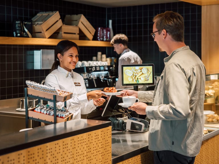 Kundenservice in einem Café mit Barista und Kunde am Tresen.