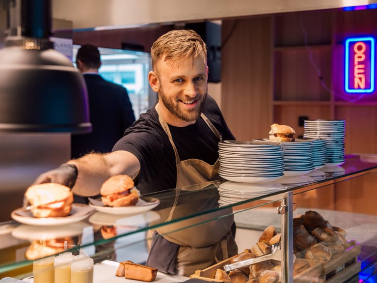 Mann reicht Teller mit Burgern in Restaurantküche aus.