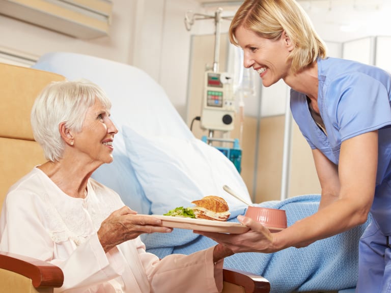 Krankenschwester serviert älterer Patientin im Krankenhauszimmer Essen.