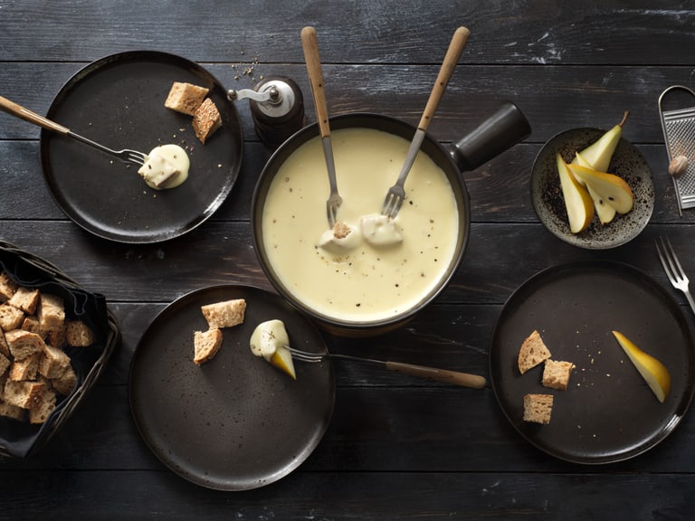 Käsefondue mit Brot und Birne auf Holztisch.