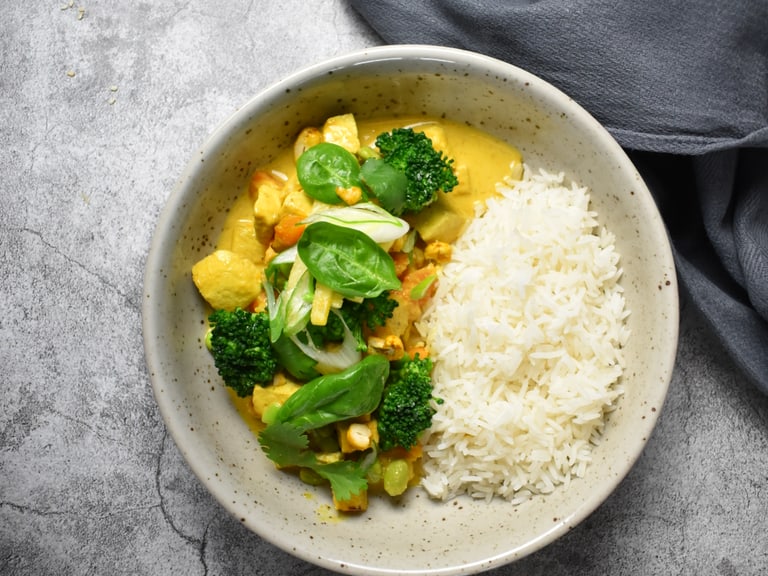 Teller mit Curry, Brokkoli und Reis auf grauem Untergrund.