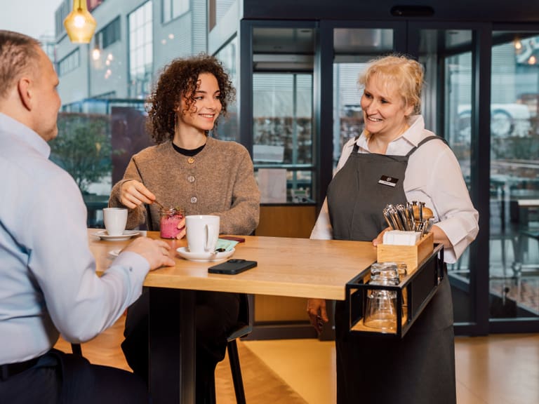 Eine Frau bedient zwei Personen an einem Café-Tisch.