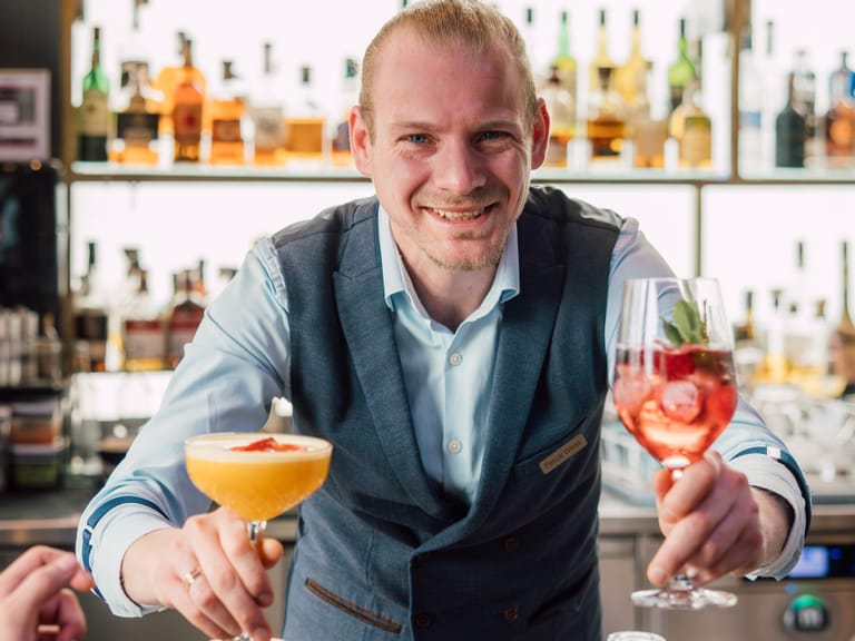 Barkeeper serviert Cocktails hinter der Bar mit Flaschen im Hintergrund.