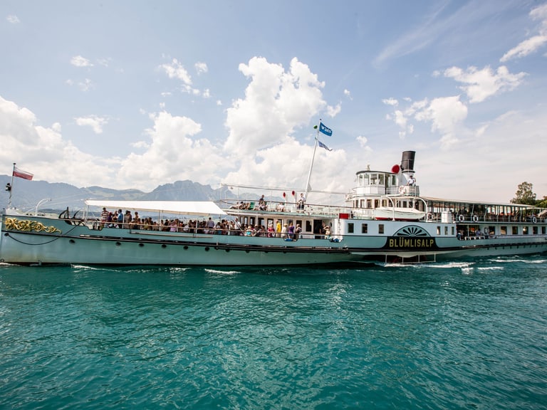 Schiff fährt auf dem See bei schönem Wetter und viele Personen sind auf dem Schiff zu sehen.