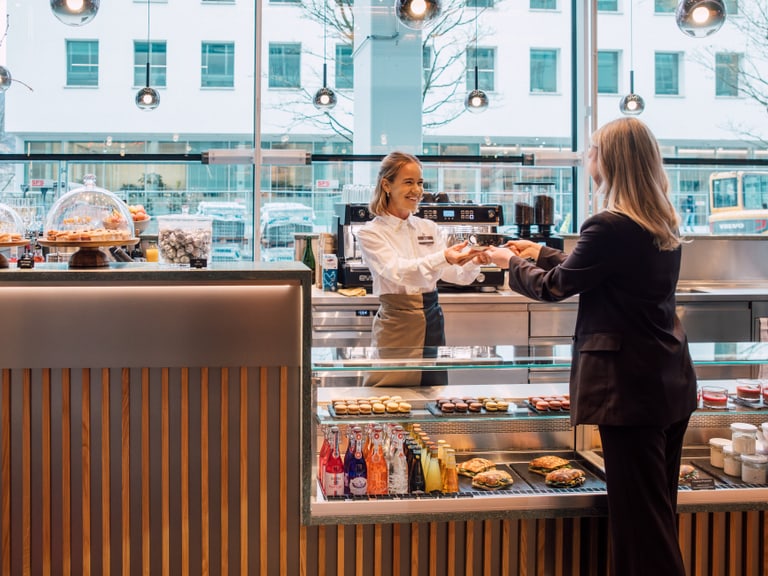 Kundin wird in einem Café bedient, Stadtansicht im Hintergrund.