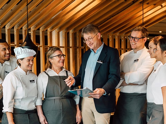 Lächelnde Hotelmitarbeiter stehen mit einem Manager in Gespräch.