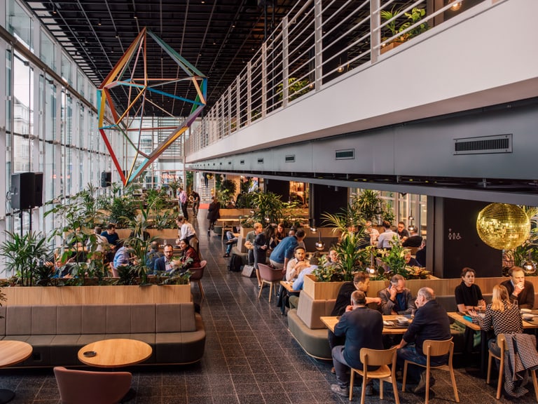 Geschäftsleute in modernem Café mit geometrischem Kunstwerk und Pflanzen.