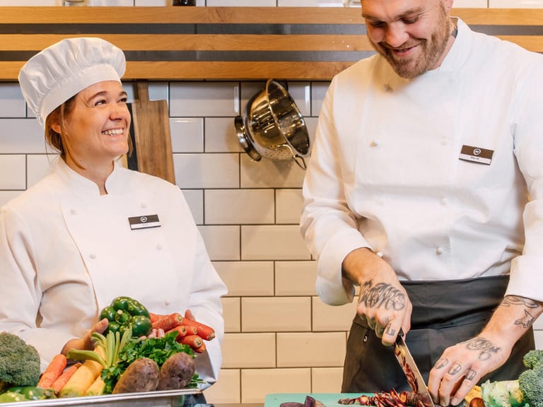 Zwei Köche schneiden Gemüse in der Küche, lachend und lächelnd.