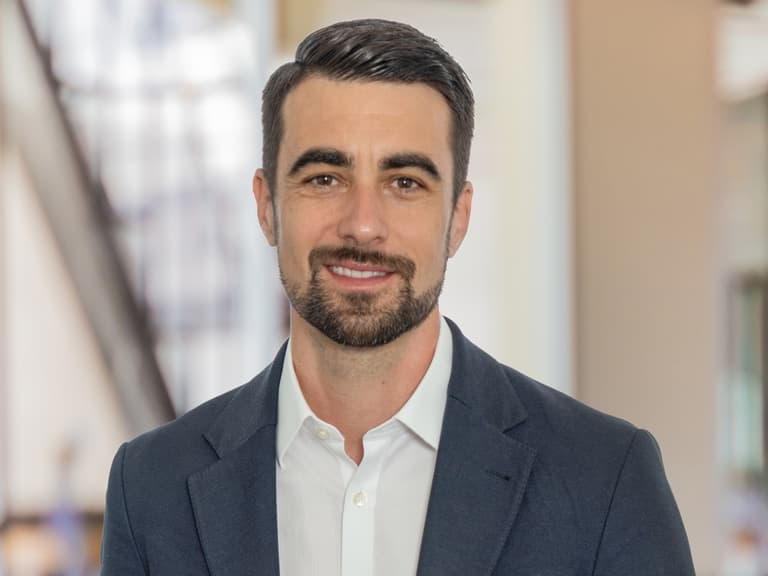 Mann in einem Anzug und mit einer Uhr in einem Bürokorridor lächelnd.