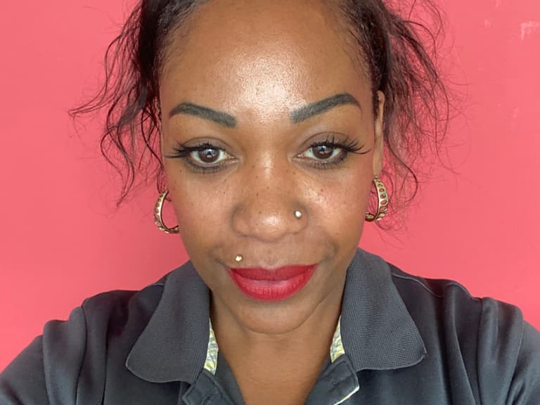 Porträt einer Frau vor rosa Hintergrund mit Namensschild.