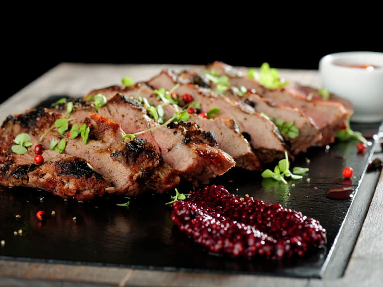 Gegrilltes Fleisch mit Kräutern und Sauce auf Holzbrett serviert.
