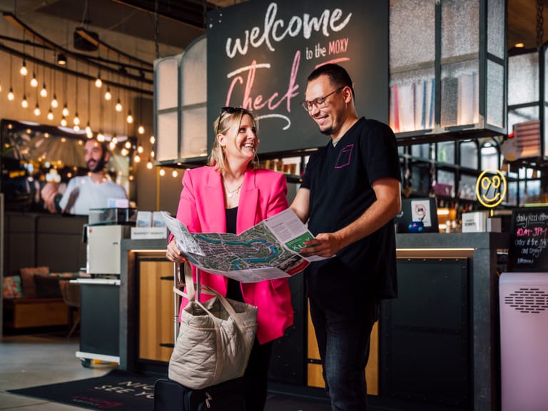 Zwei Menschen schauen auf eine Karte in einer Hotellobby mit Willkommensschild.