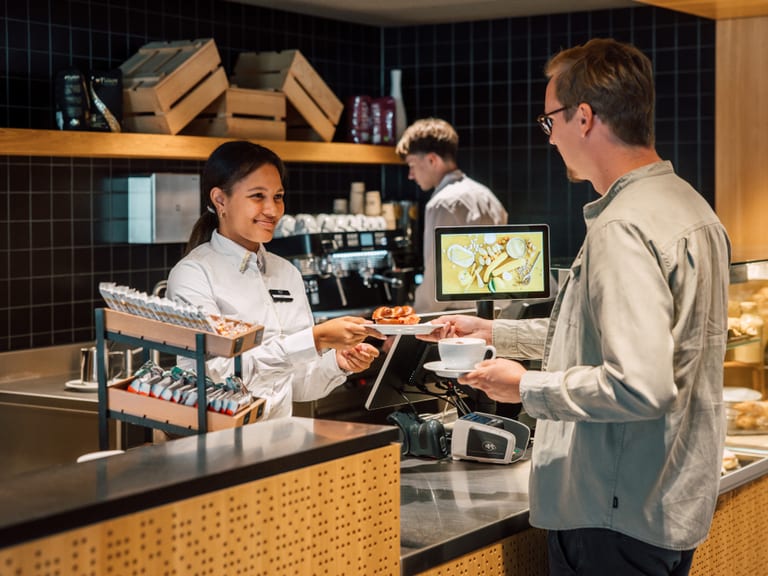 Person bestellt Kaffee beim Barista in einem modernen Café.