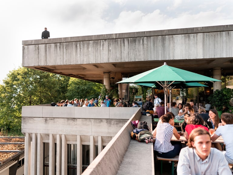 Leute im Restaurant im Freien auf einem Balkon mit Sonnenschirm.