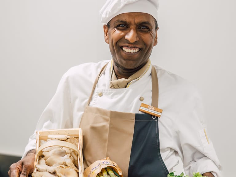 Lächelnder Koch hält Tablett mit frischen Zutaten.