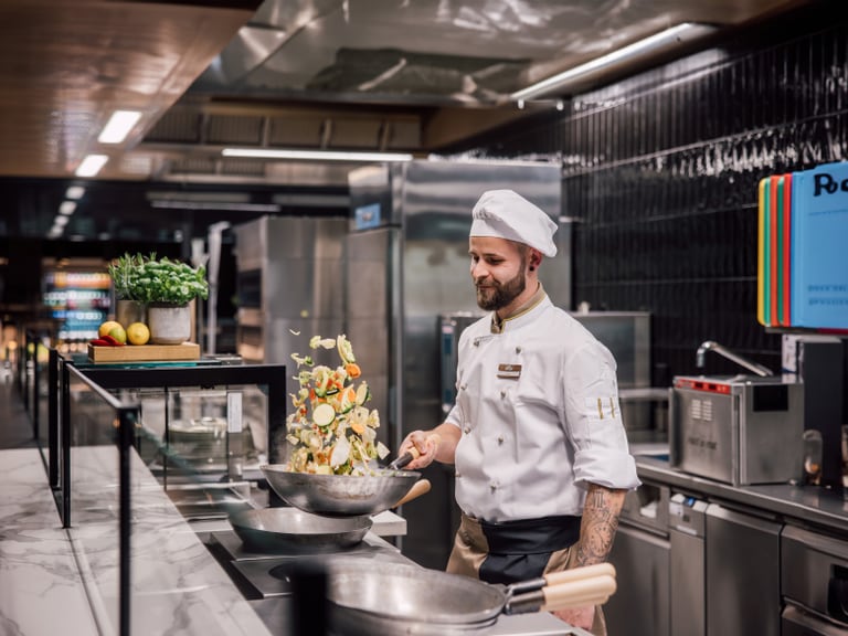 Koch in Restaurantküche wirft Gemüse in der Pfanne.