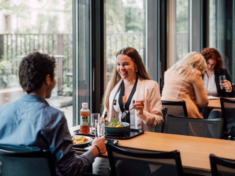 Zwei Personen essen zusammen an einem Tisch im Restaurant, zwei weitere Personen sitzen im Hintergrund.