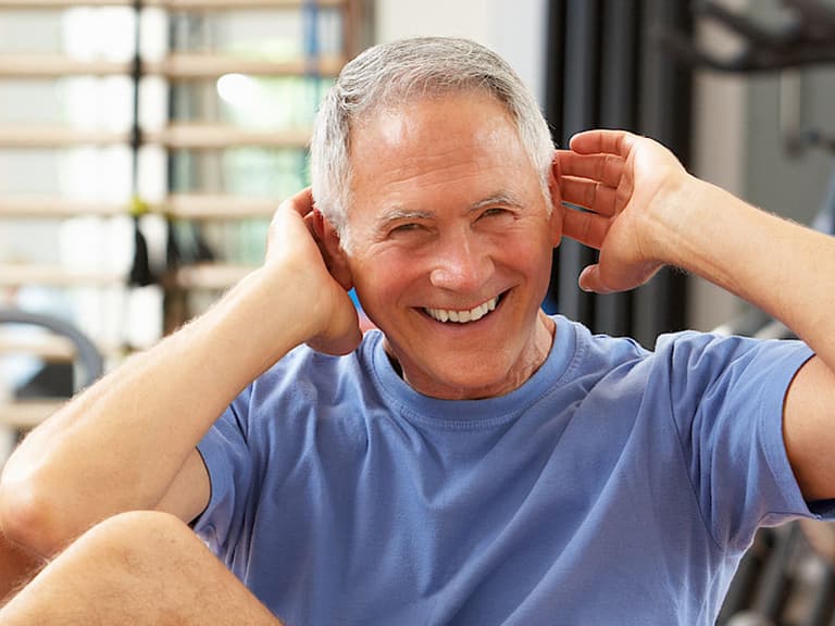 Älterer Mann lächelt beim Training im Fitnessstudio.