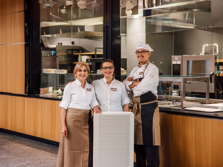 Drei Restaurantmitarbeiter lächelnd vor einer Küche.