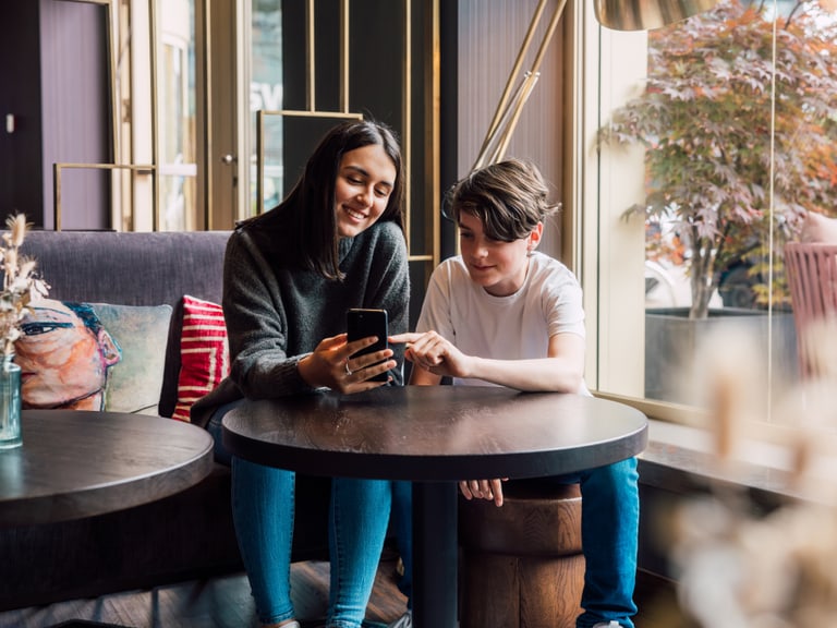 Zwei Personen, die in einem Café auf ein Smartphone schauen.