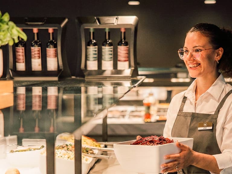 Lächelnde Frau mit Schüssel an Salatbuffet.
