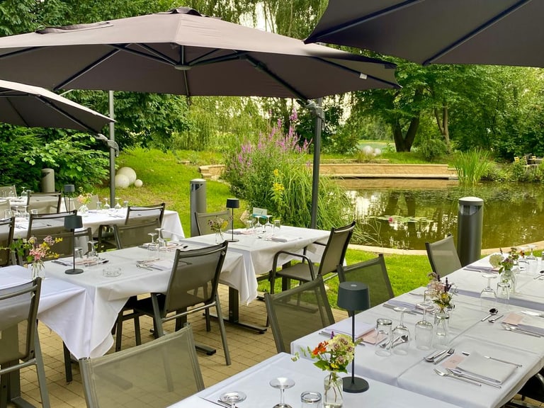 Gedeckte Aussenterrasse mit Teich und Sonnenschirmen.