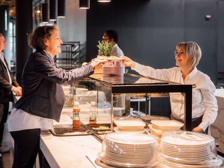 Zwei Frauen geben sich an einem Restaurantbuffet eine Pflanze.