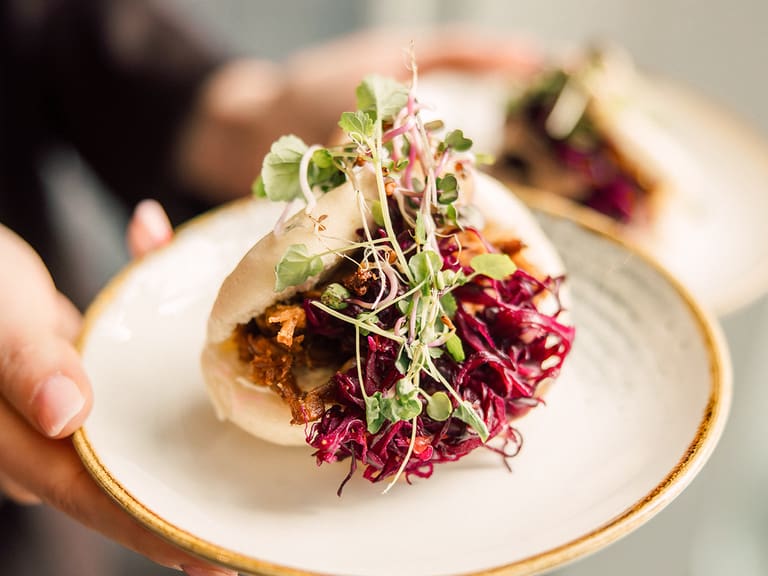 Person hält Teller mit gefülltem Bao-Brötchen und Kräutern.