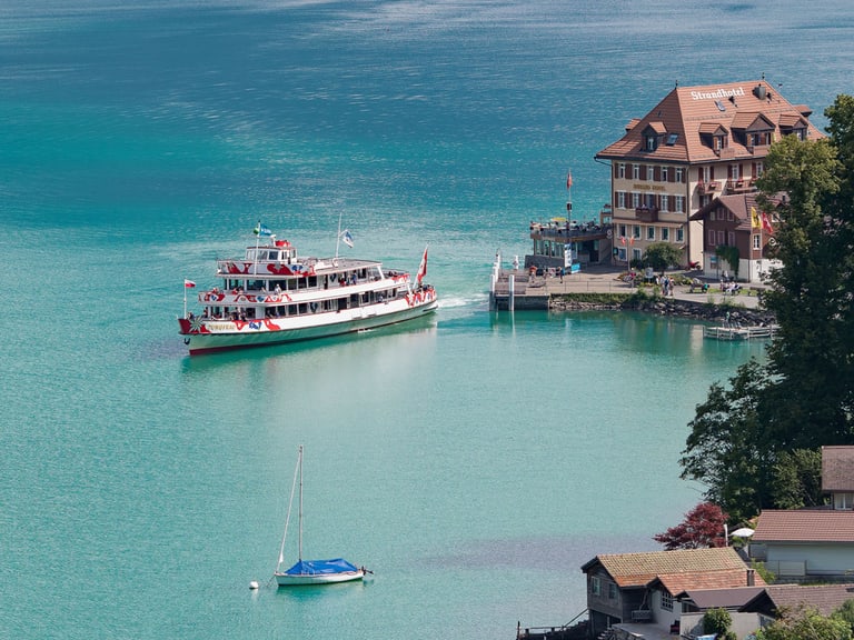 Ein Schiff fährt bei sonnigem Wetter vom Hafen weg auf dem Brienzersee.