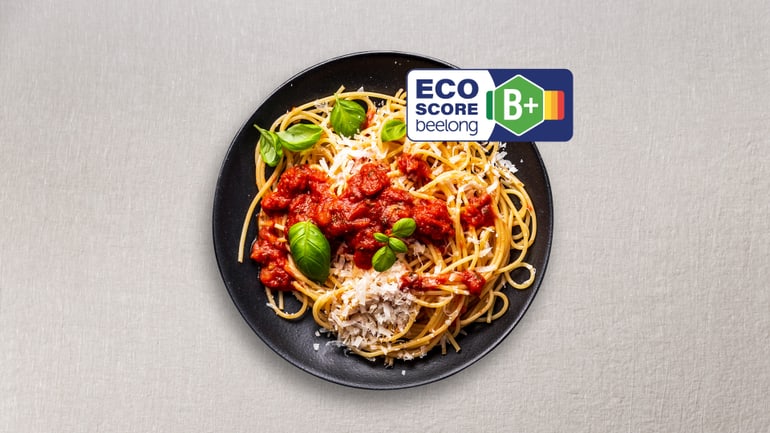 Schwarzer Teller mit Spaghetti, Tomatensauce, Basilikum und Eco-Score-Label B+.",